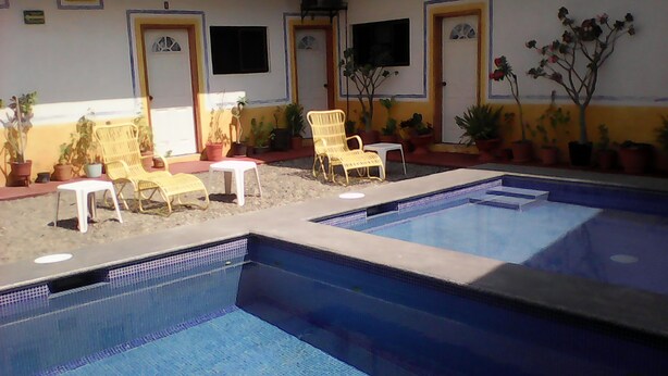 A pool area with multiple chairs and a small table, surrounded by potted plants. - Hotel Sarabi Barra de Navidad (Barra de Navidad)