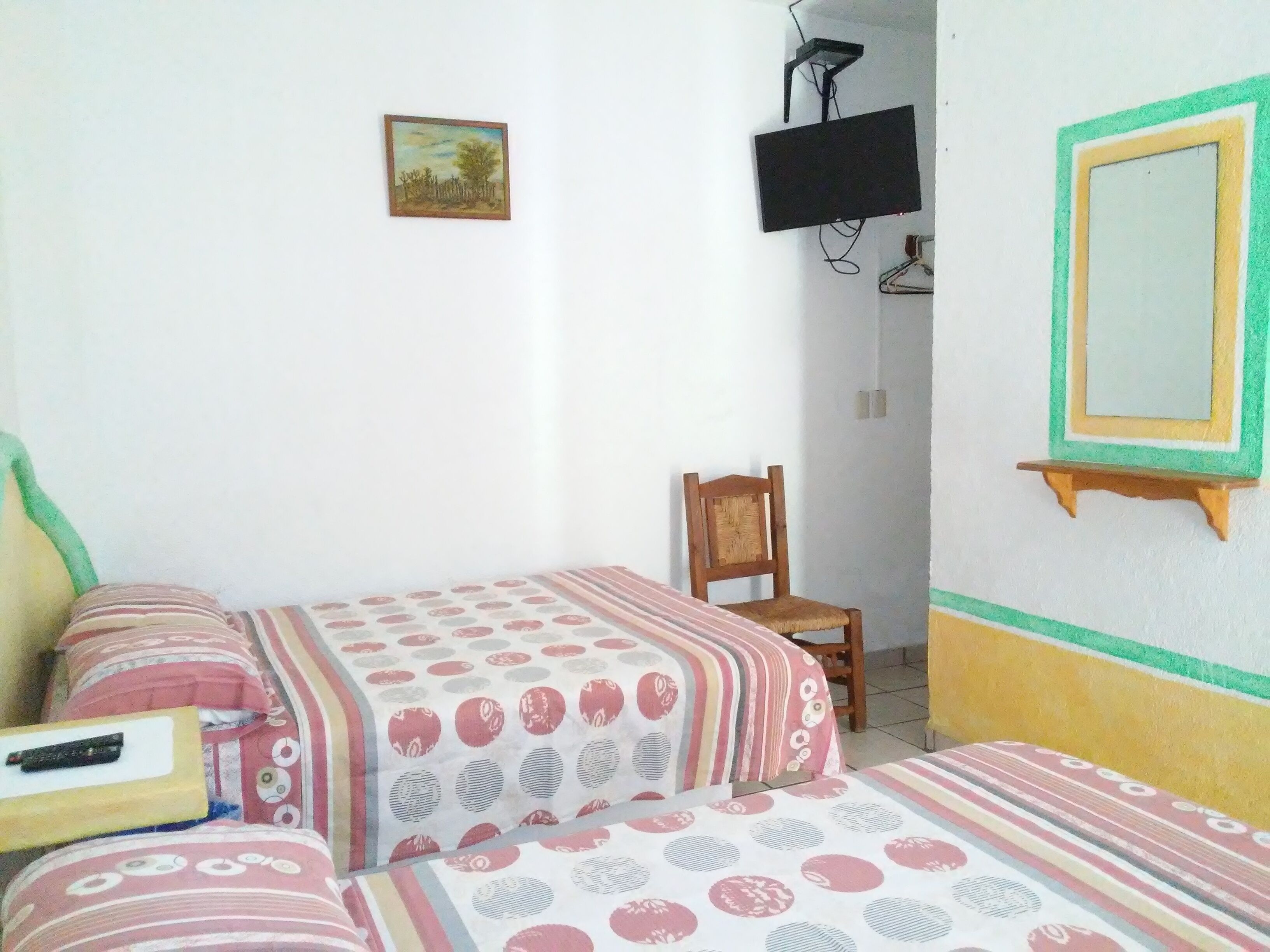 A bedroom with two beds, a chair, a TV, and a small painting on the wall.