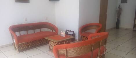 A living room with a sofa set, a coffee table, and two chairs. There are two framed pictures on the wall.