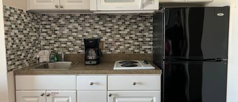 A kitchen with white cabinets, a black refrigerator, a microwave, a coffee maker, and a tiled backsplash.