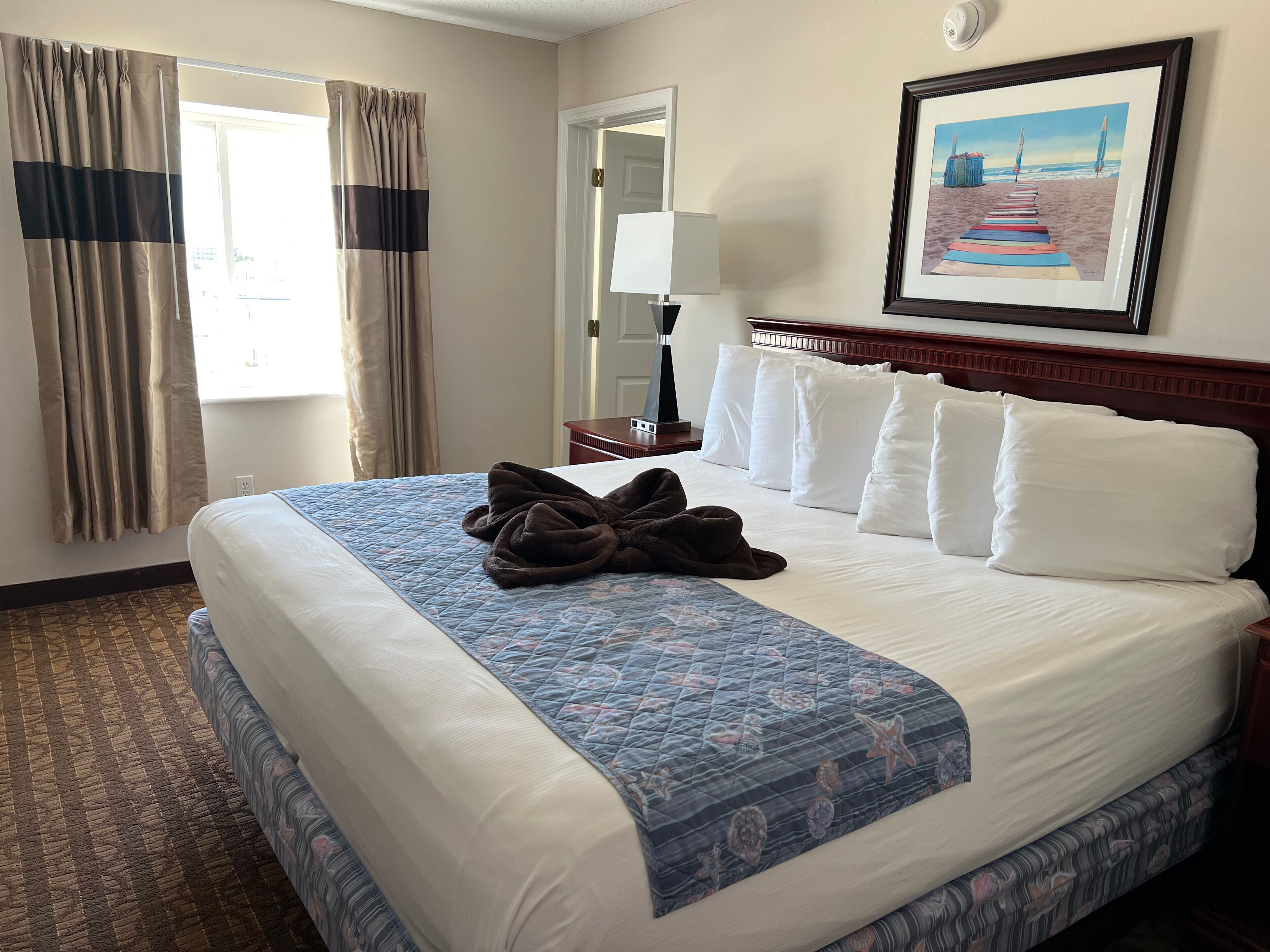 A hotel room with a large bed, a headboard, a framed picture on the wall, and a window with curtains.