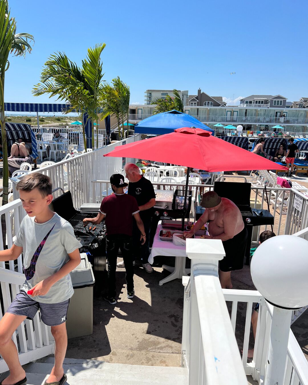 A beachside restaurant with outdoor seating, a grill, and umbrellas.