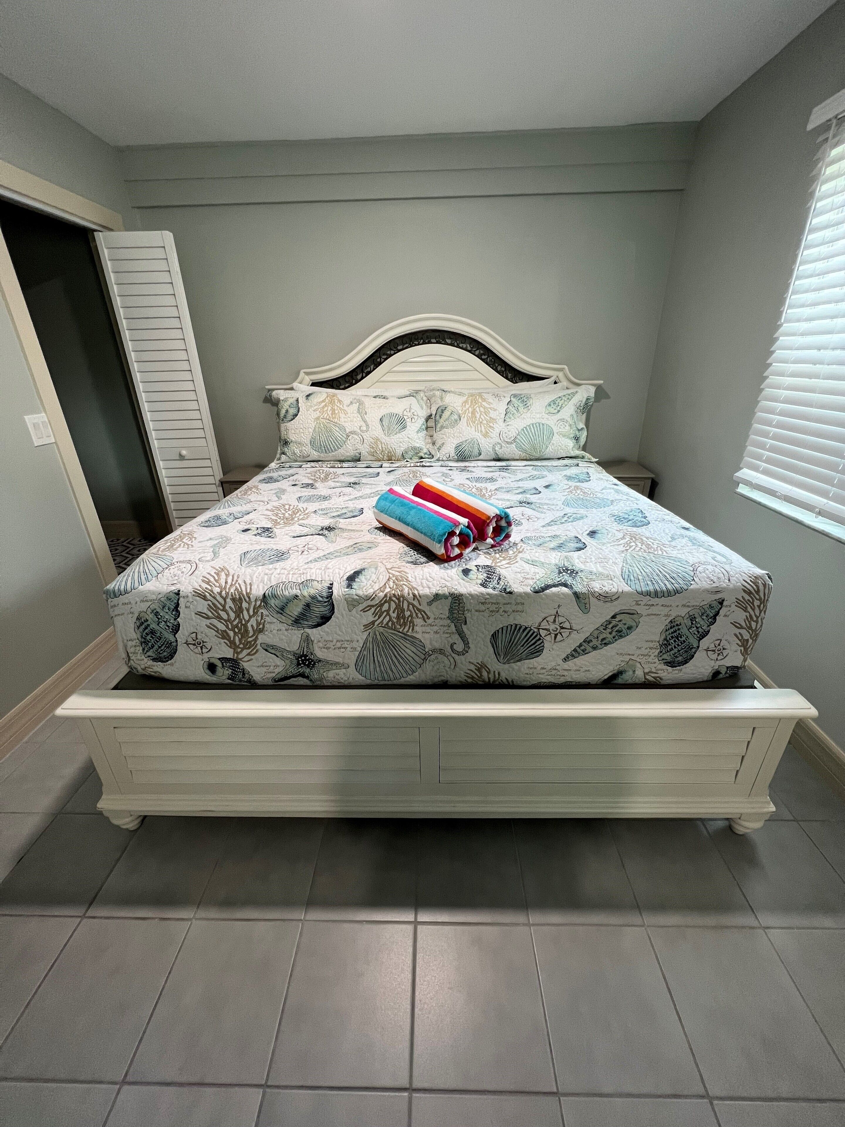 A bed with a floral bedspread, a headboard, and a pair of rolled towels.