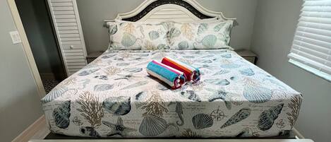 A bed with a floral bedspread, a headboard, and a pair of rolled towels.