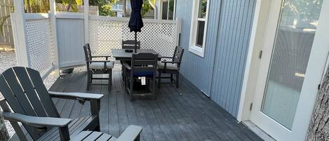 A deck with a table and chairs, a covered grill, and a white fence.