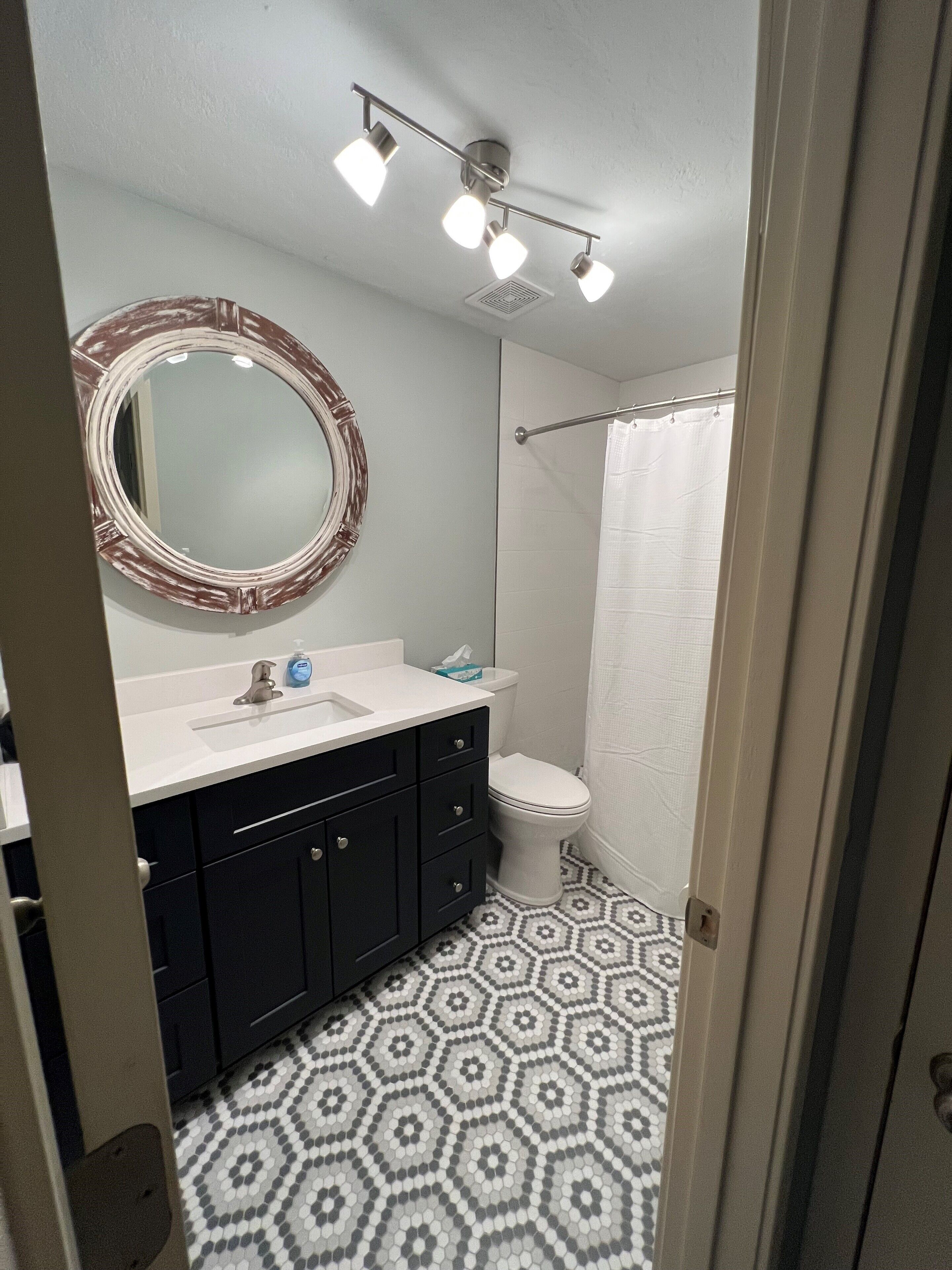 Une salle de bain avec un meuble-lavabo noir, un miroir rond, des toilettes blanches et un rideau de douche.
