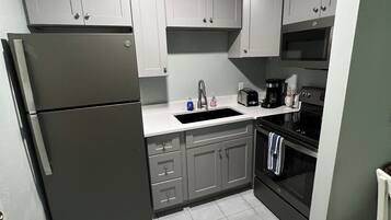 A kitchen with grey cabinets, a black refrigerator, a sink, a stove, and a microwave.