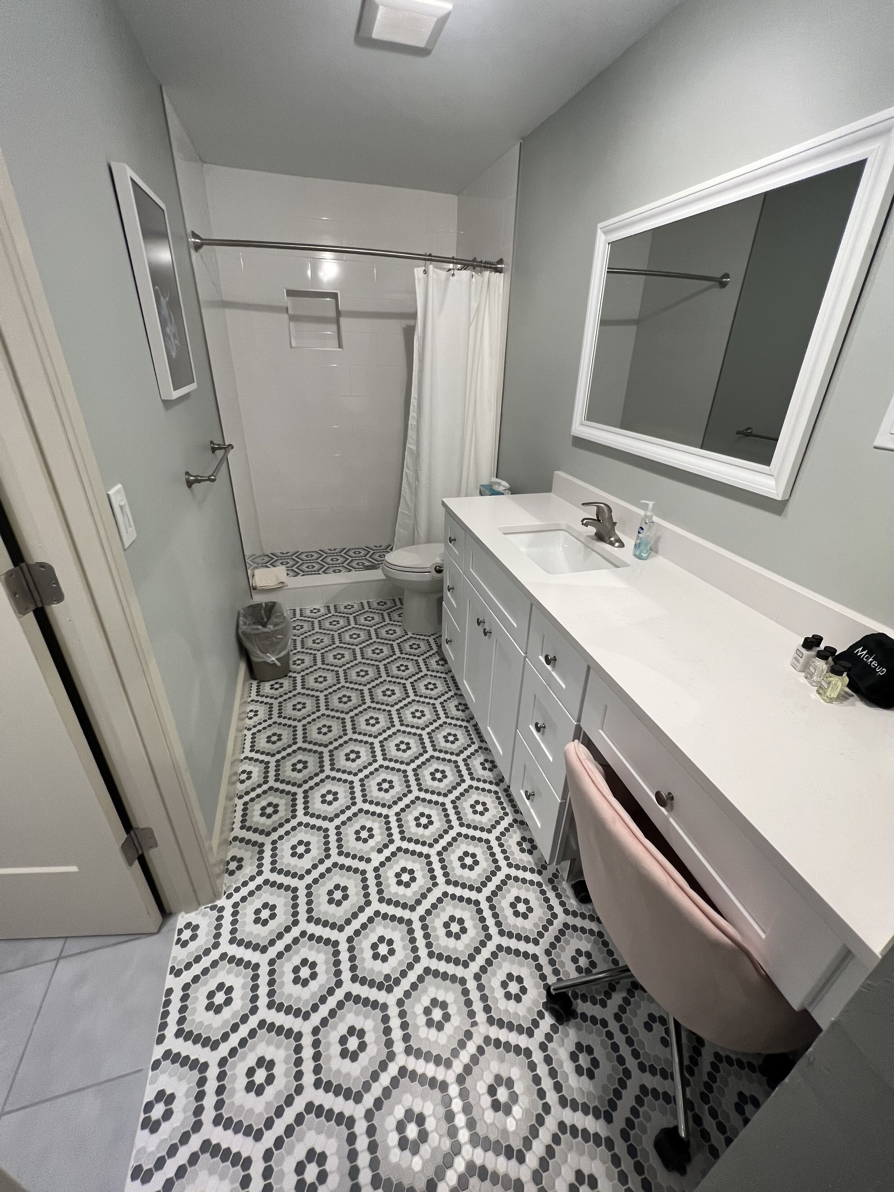 Een badkamer met een witte wastafel, spiegel en toilet. De vloer heeft een geometrisch tegelpatroon.
