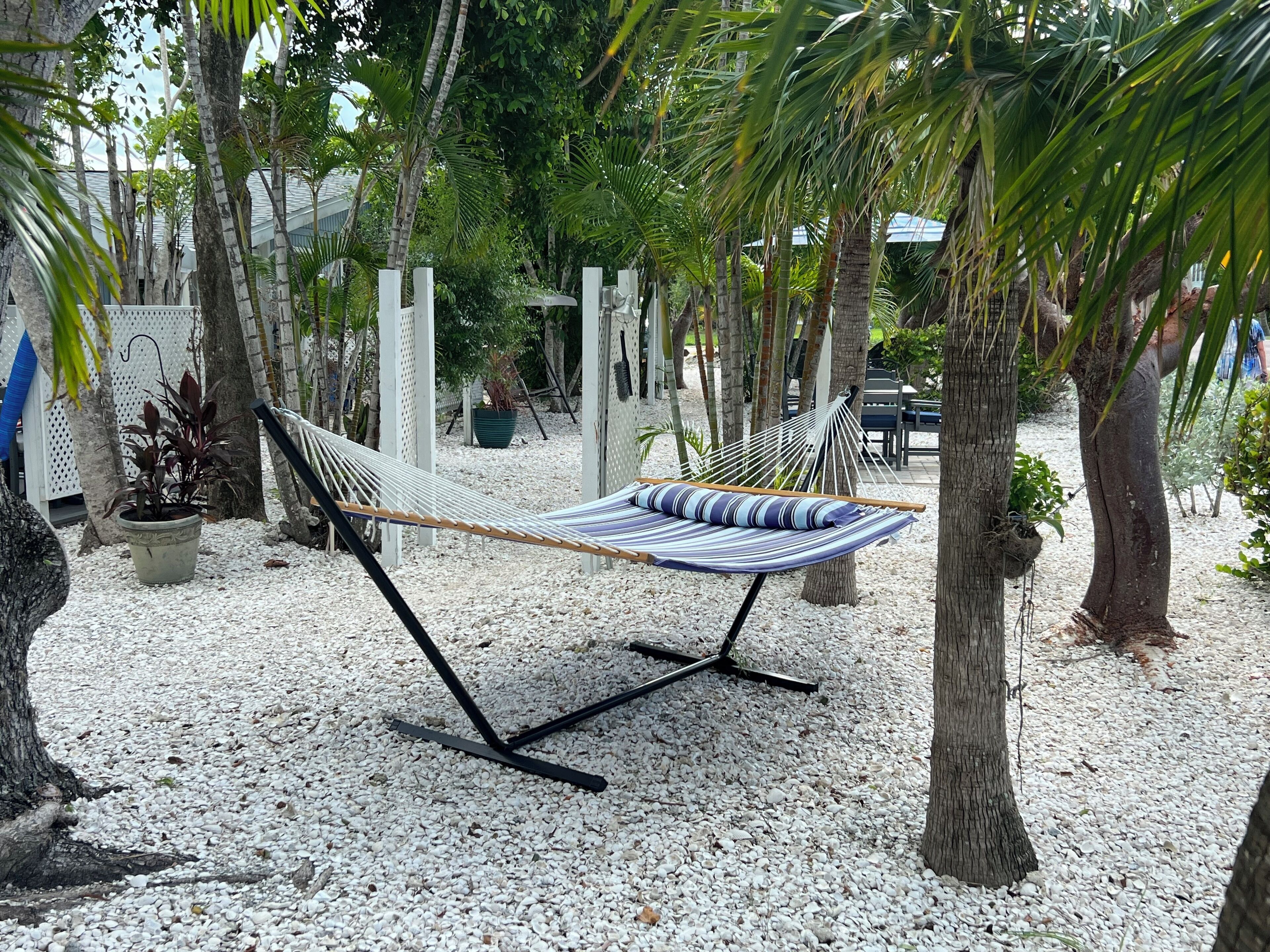 A hammock set up on a gravel surface surrounded by trees and potted plants.