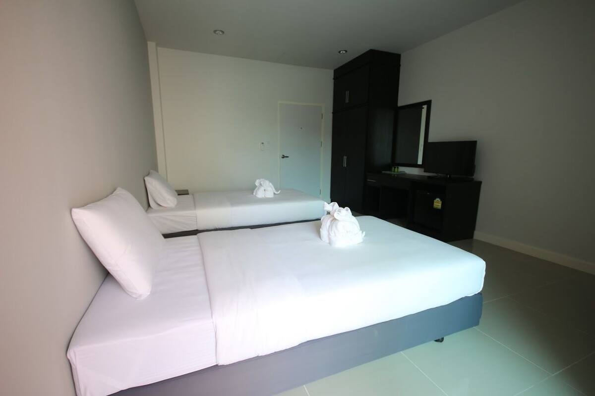 Habitación de hotel con dos camas individuales, un armario de color oscuro, un televisor de pantalla plana y una puerta al fondo.