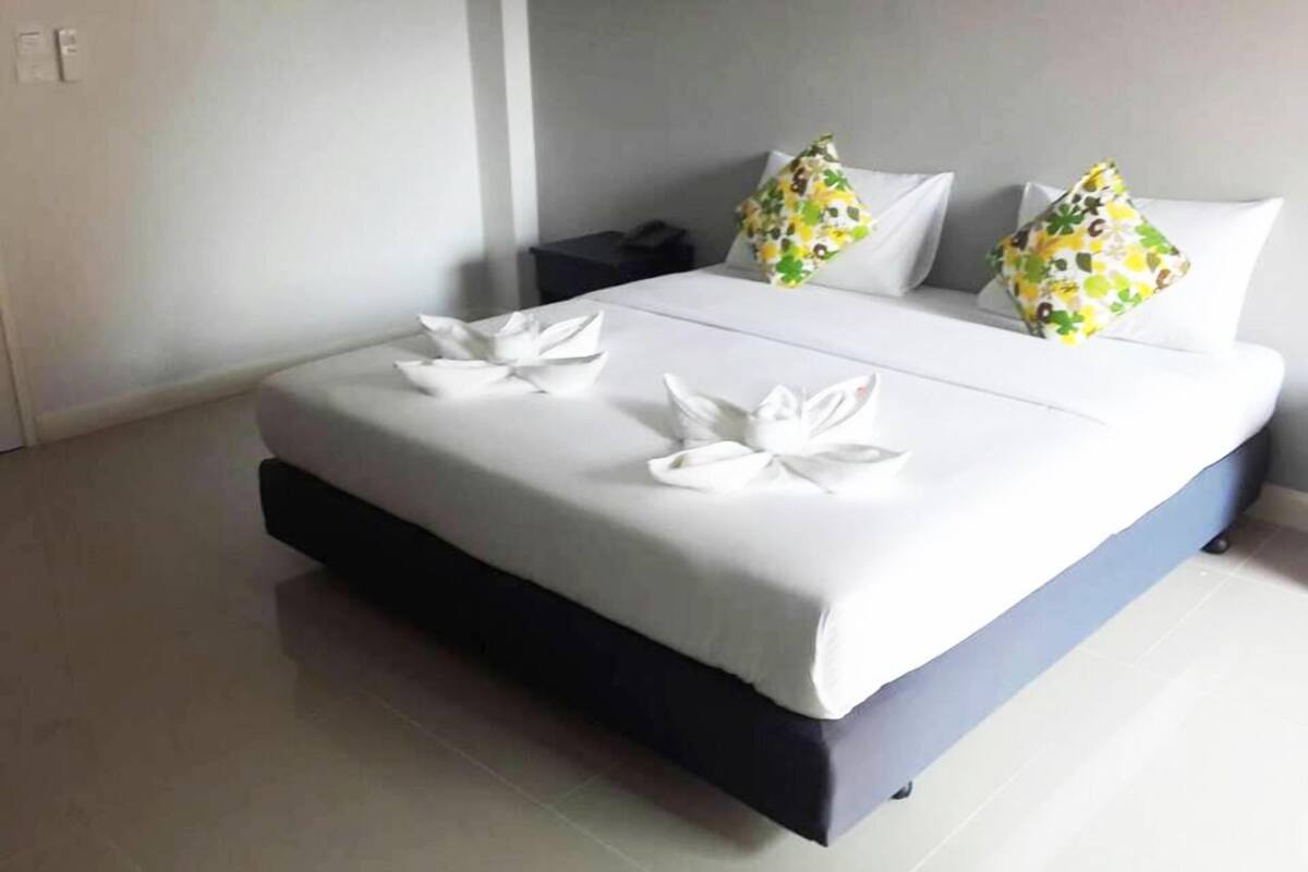 Una cama bien hecha con sábanas blancas y almohadones decorativos, una mesita de noche y una pared lisa.