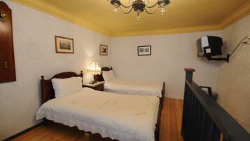 A bedroom with two single beds, a wooden floor, a chandelier, and a television mounted on the wall.