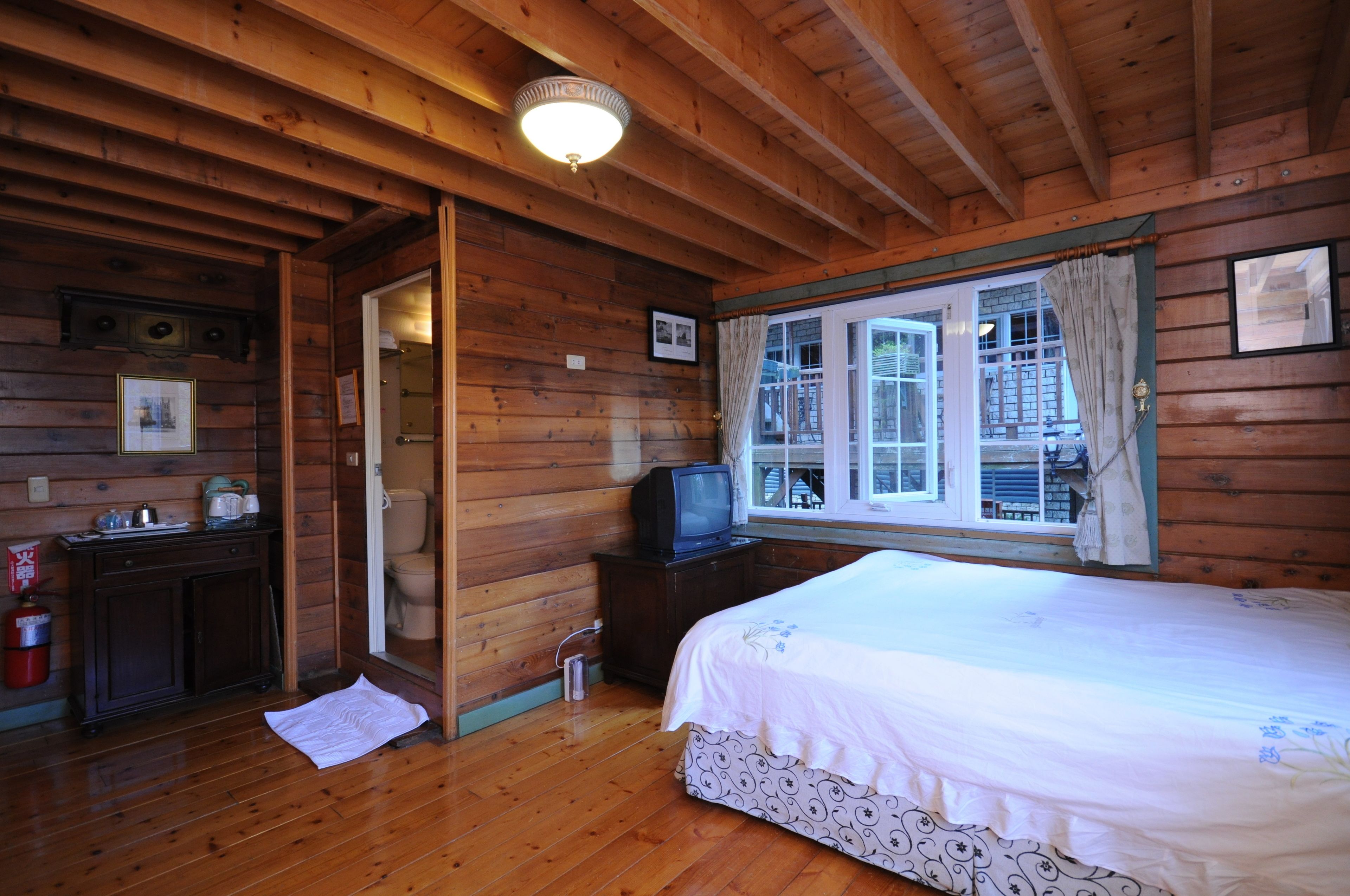 Une chambre à coucher située dans une cabane en bois, comprenant un lit, un téléviseur, une fenêtre avec des rideaux et une porte donnant sur une autre pièce.