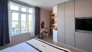 Une chambre d’hôtel avec un grand lit, un bureau avec une chaise, une coiffeuse avec un miroir, un téléviseur fixé au mur et une fenêtre avec des rideaux.