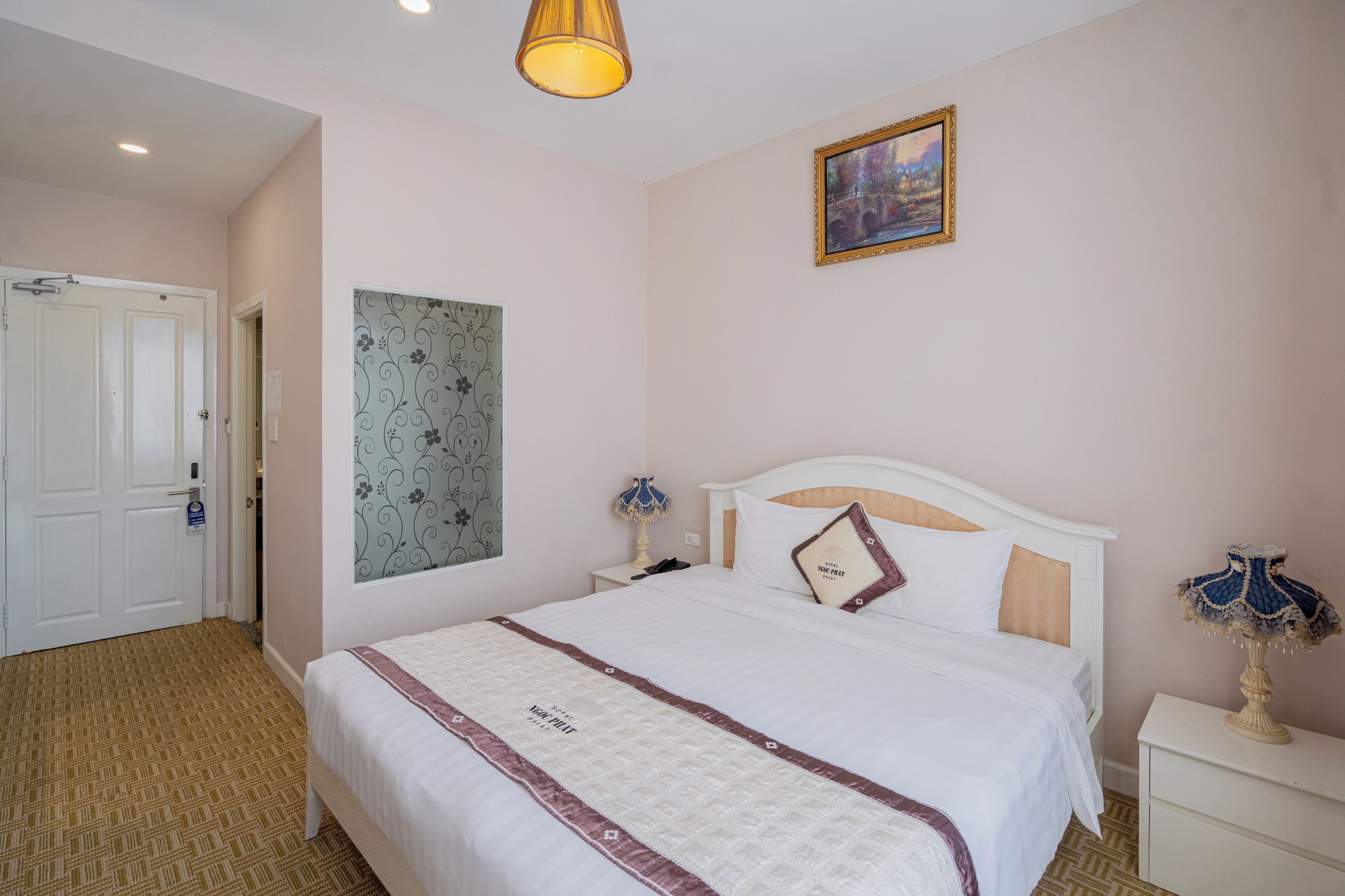 A bedroom with a bed, nightstands, a lamp, a painting, and a door.