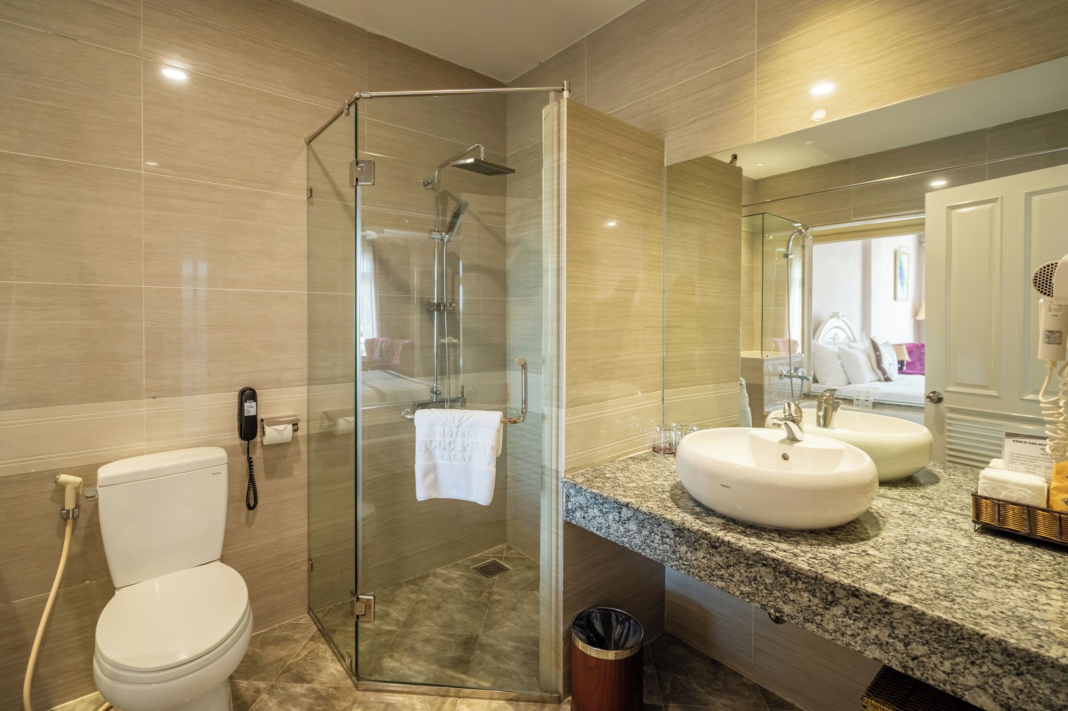Une salle de bain moderne avec une douche à parois de verre, des toilettes blanches et un comptoir en granit doté de deux vasques.