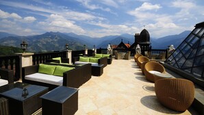 Una terraza en la azotea con mobiliario de mimbre, vistas a montañas y un edificio con techo abovedado.