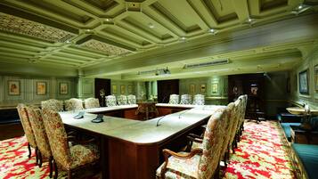 Une salle de conférence avec une longue table, des chaises recouvertes d’un tissu à motifs floraux et un tapis rouge à motifs.