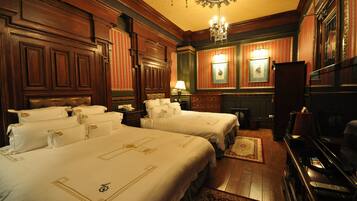 A hotel room with two beds, wooden paneling, a chandelier, a piano, and a television.