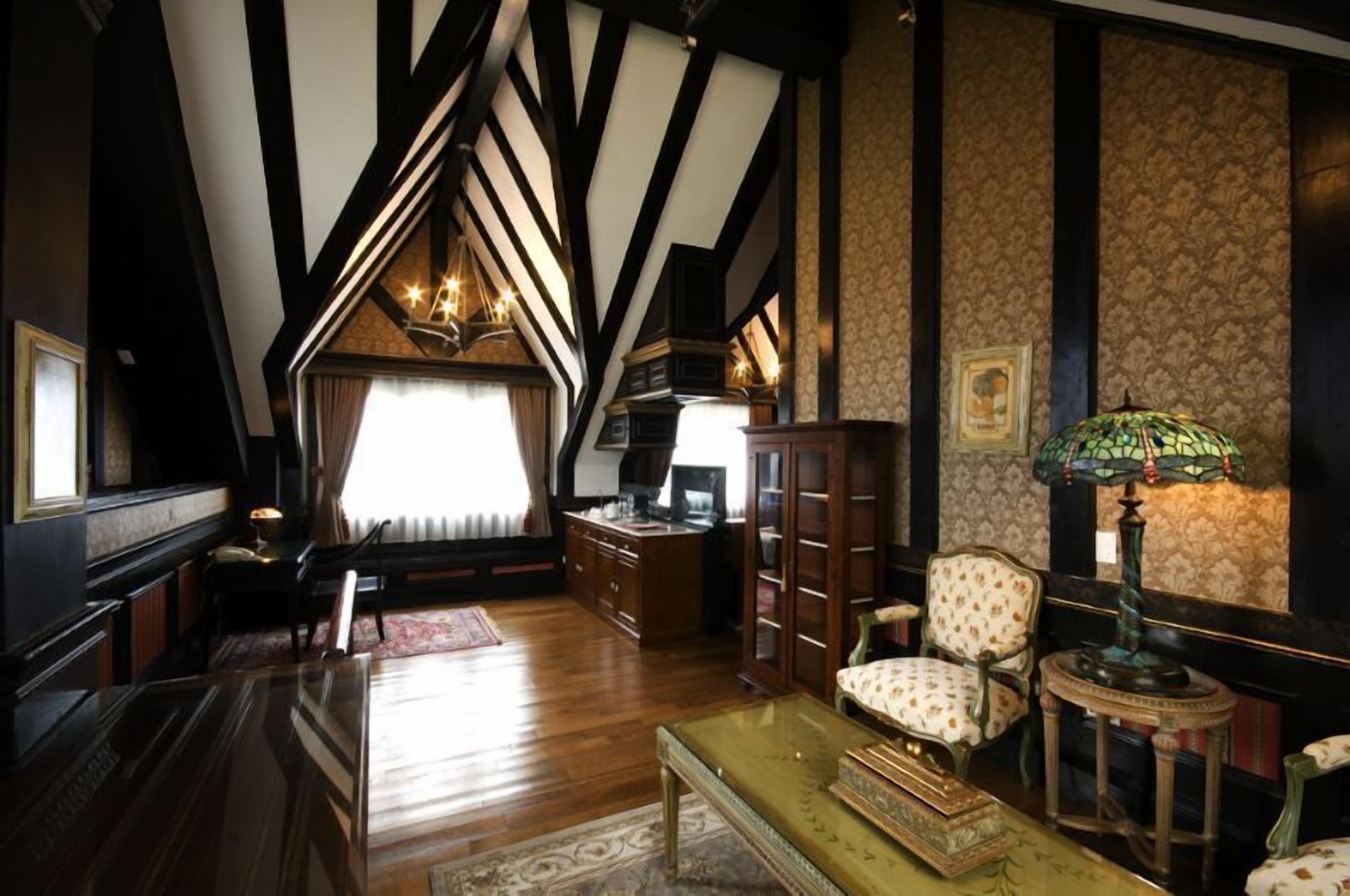 A room with exposed wooden beams, a piano, a desk, a chair, and a lamp.