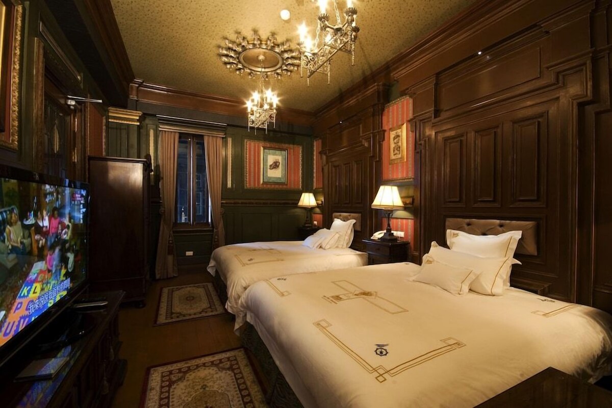 A hotel room with two beds, a television, and a chandelier.