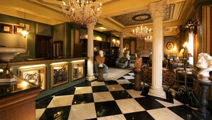 Un vestíbulo lujoso con piso a cuadros, candelabros ornamentados y esculturas clásicas.
