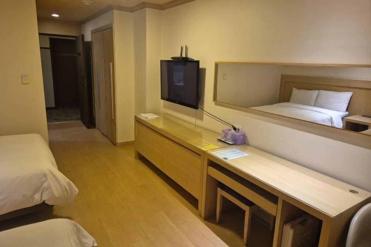 Quarto de hotel com uma cama, uma escrivaninha com computador, televisão e espelho.