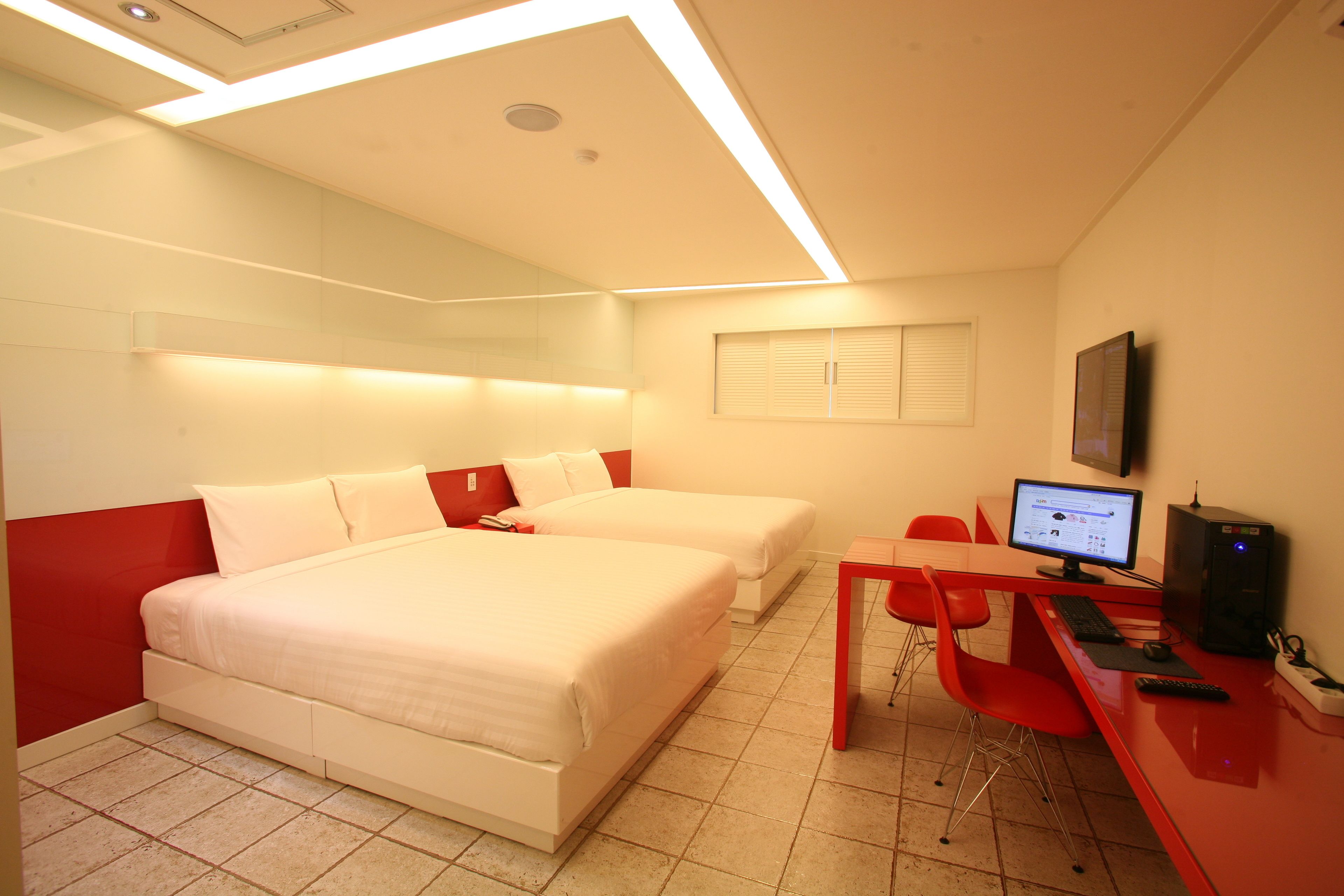 A hotel room with two beds, a desk with a computer, and a red chair.