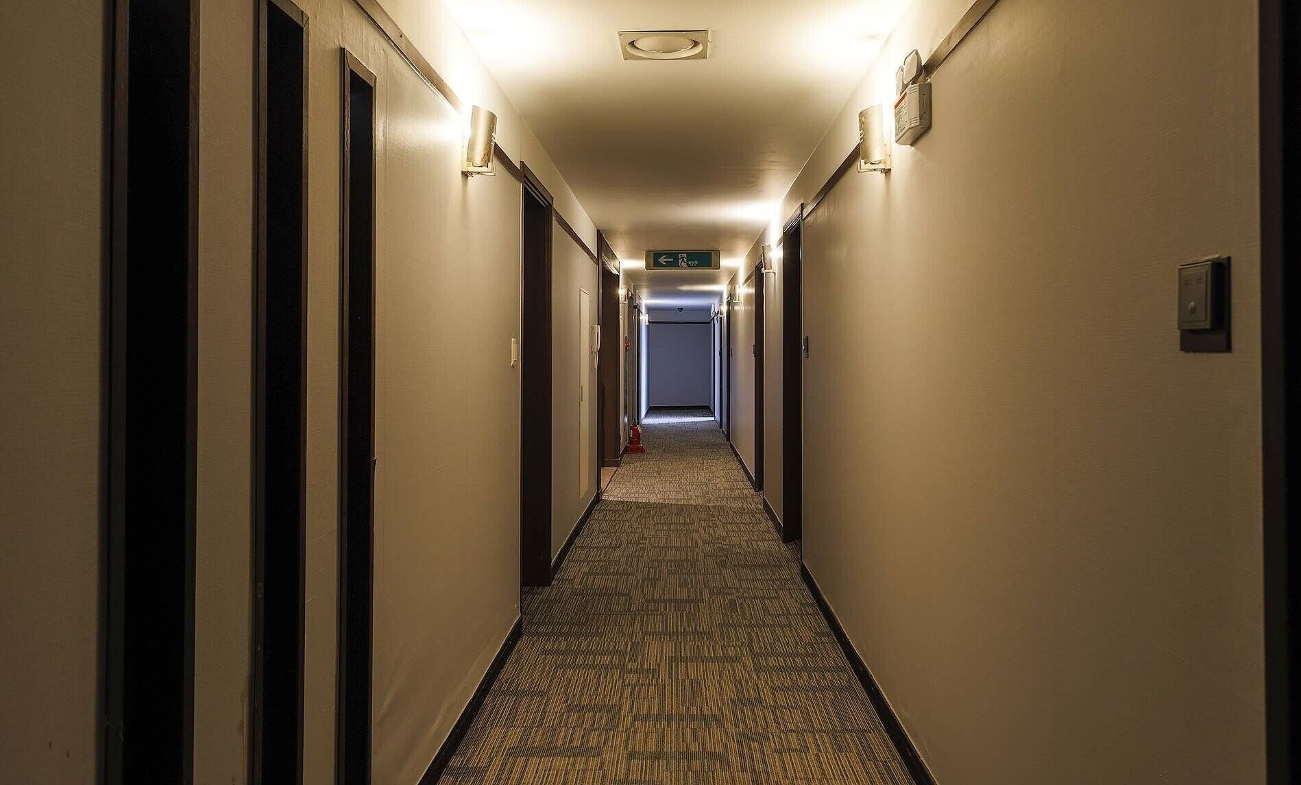 A long, narrow hotel hallway with carpeted floors, doors on both sides, and overhead lighting.