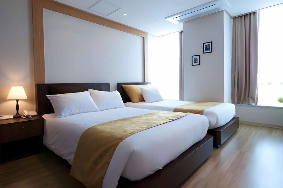 A hotel room with two beds, a nightstand with a lamp, and a window with curtains.