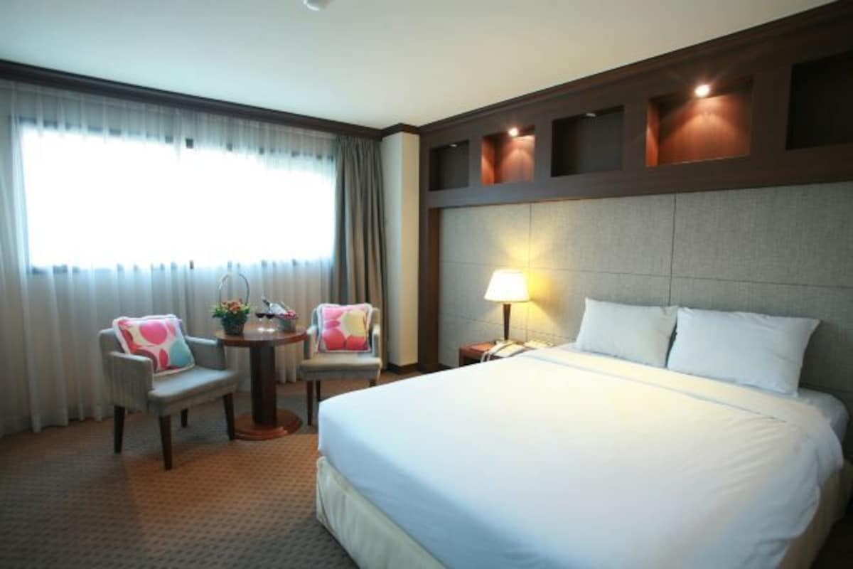 A hotel room with a large bed, two armchairs, a small table, and a lamp.