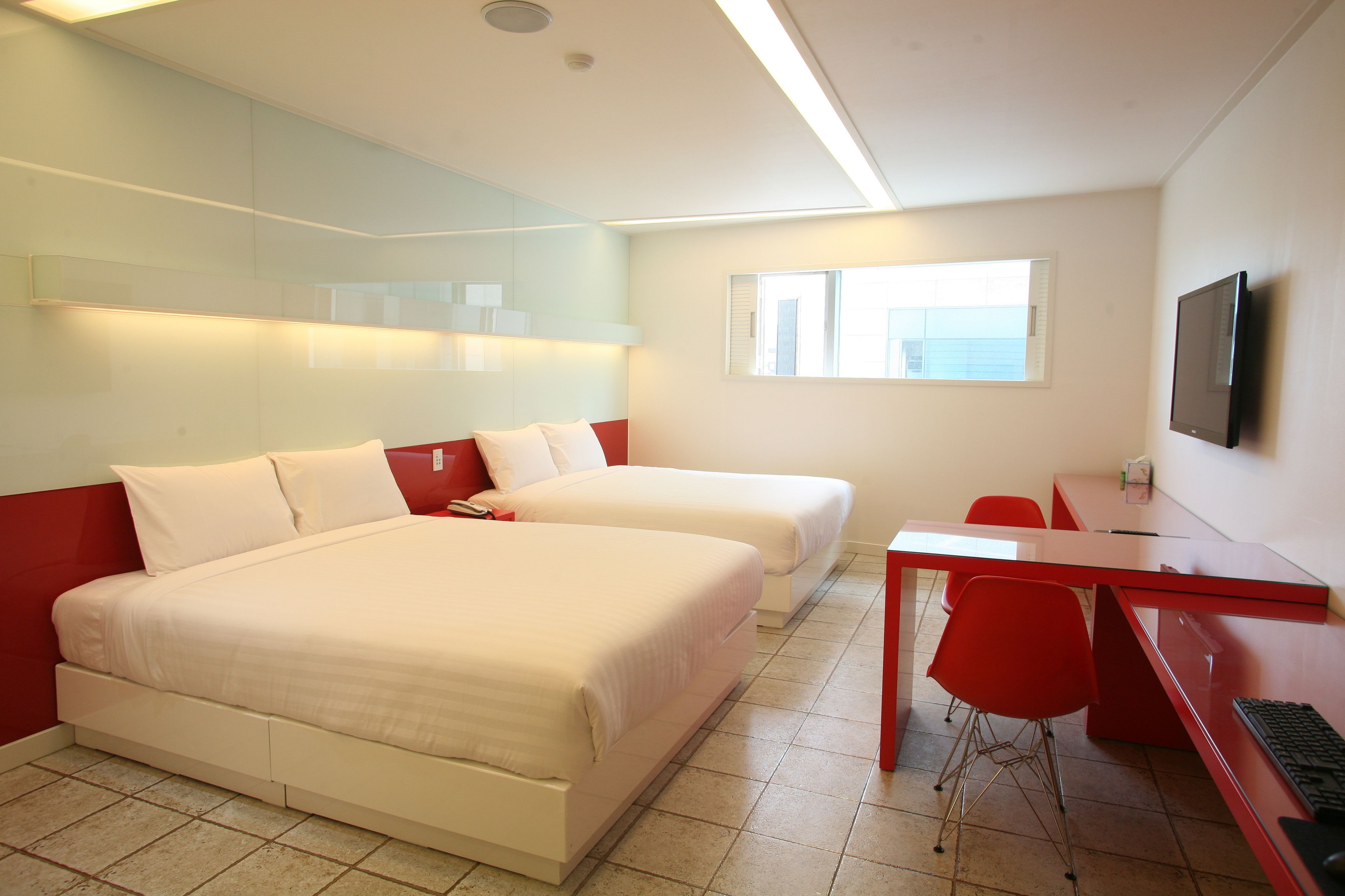 A hotel room with two beds, a desk, a chair, a TV, and a window.