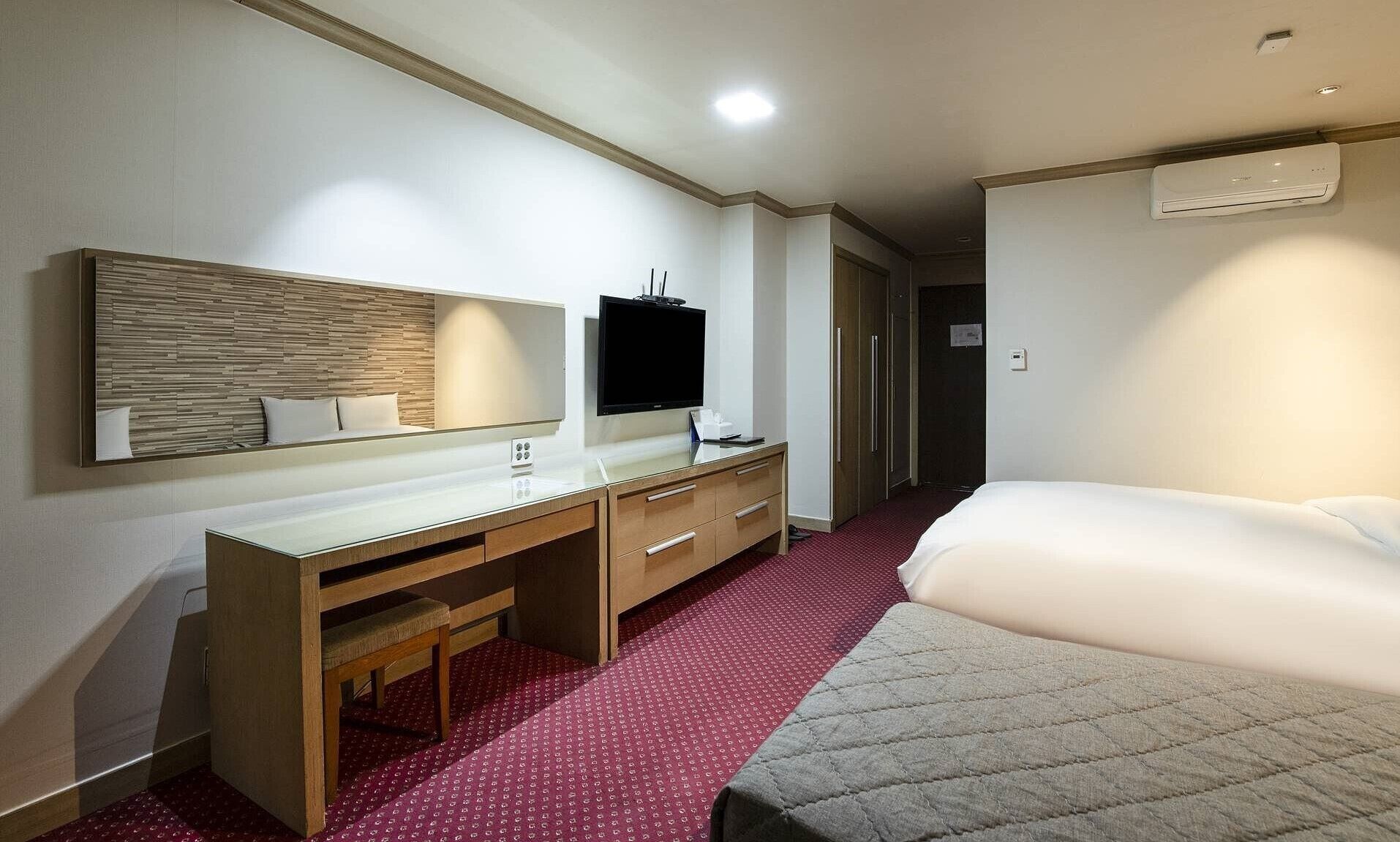 A hotel room with a bed, a desk with a chair, a television, and a large mirror.