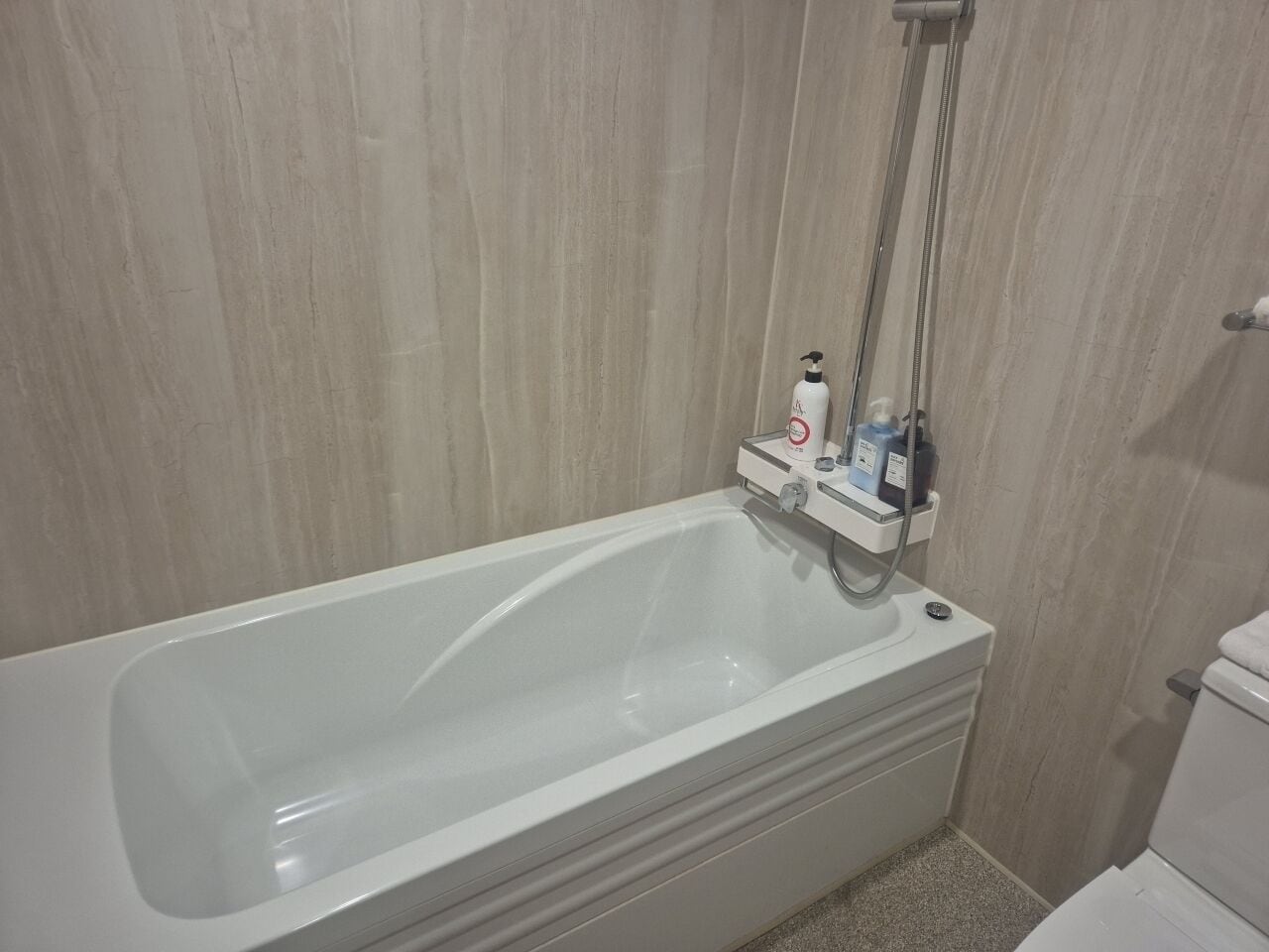 A bathroom with a white bathtub, a showerhead, and a soap dispenser.
