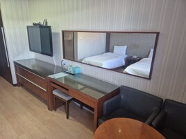Une chambre d’hôtel comprenant un lit, un bureau avec une chaise, une petite table, un miroir et un téléviseur.