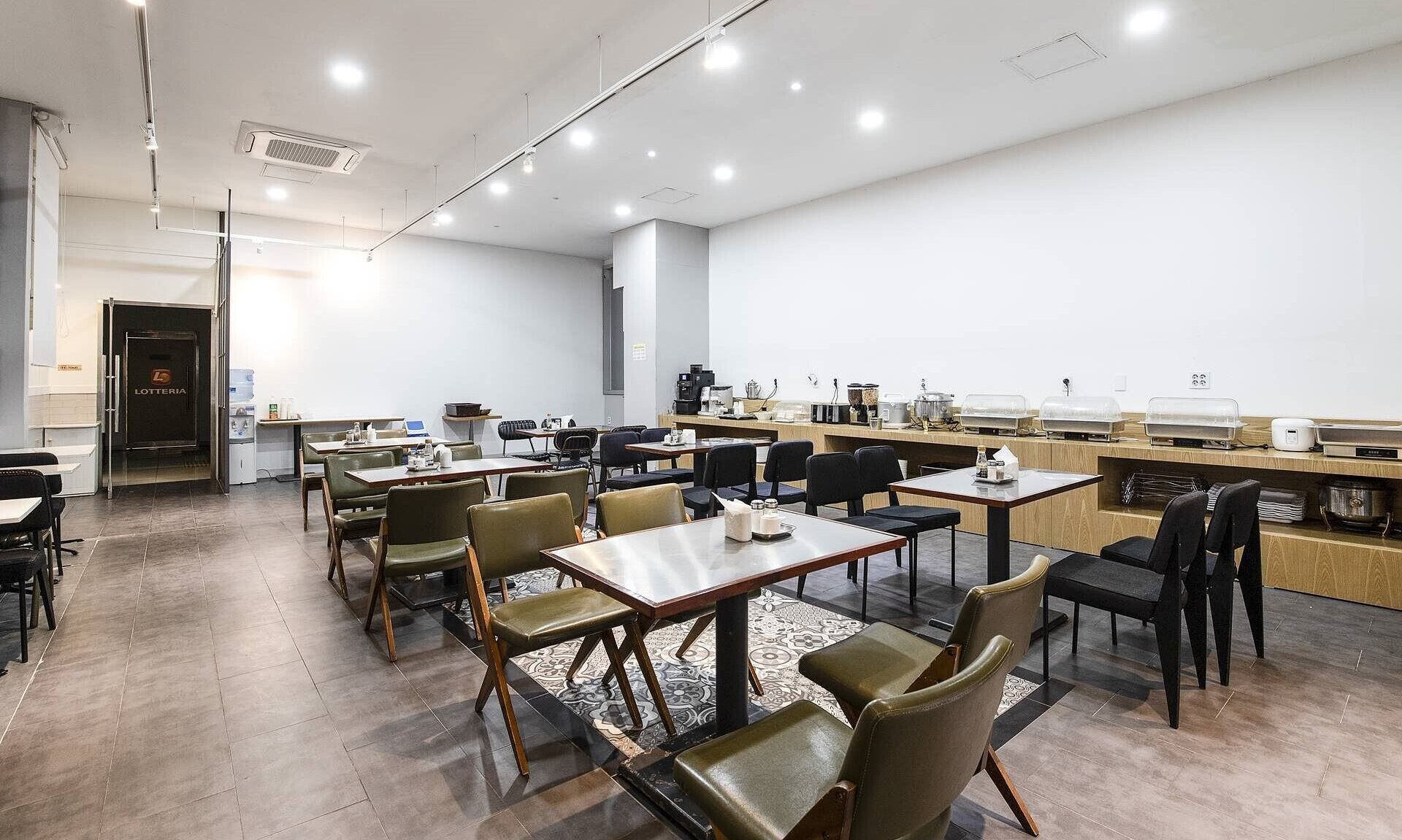 Un moderno comedor con varias mesas y sillas, una barra de buffet y una entrada visible que dice "LOTTERIA".