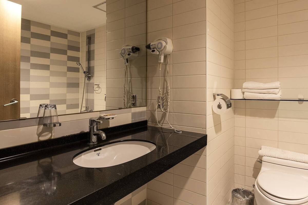 A bathroom with a sink, mirror, towel rack, shower, and toilet.