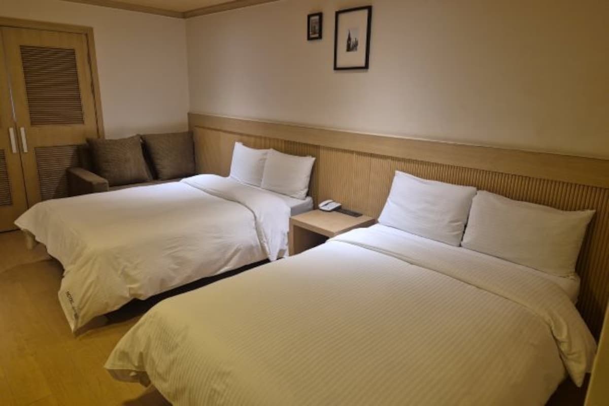 A hotel room with two beds, a wooden headboard, a bedside table with a phone, and a door with a window.