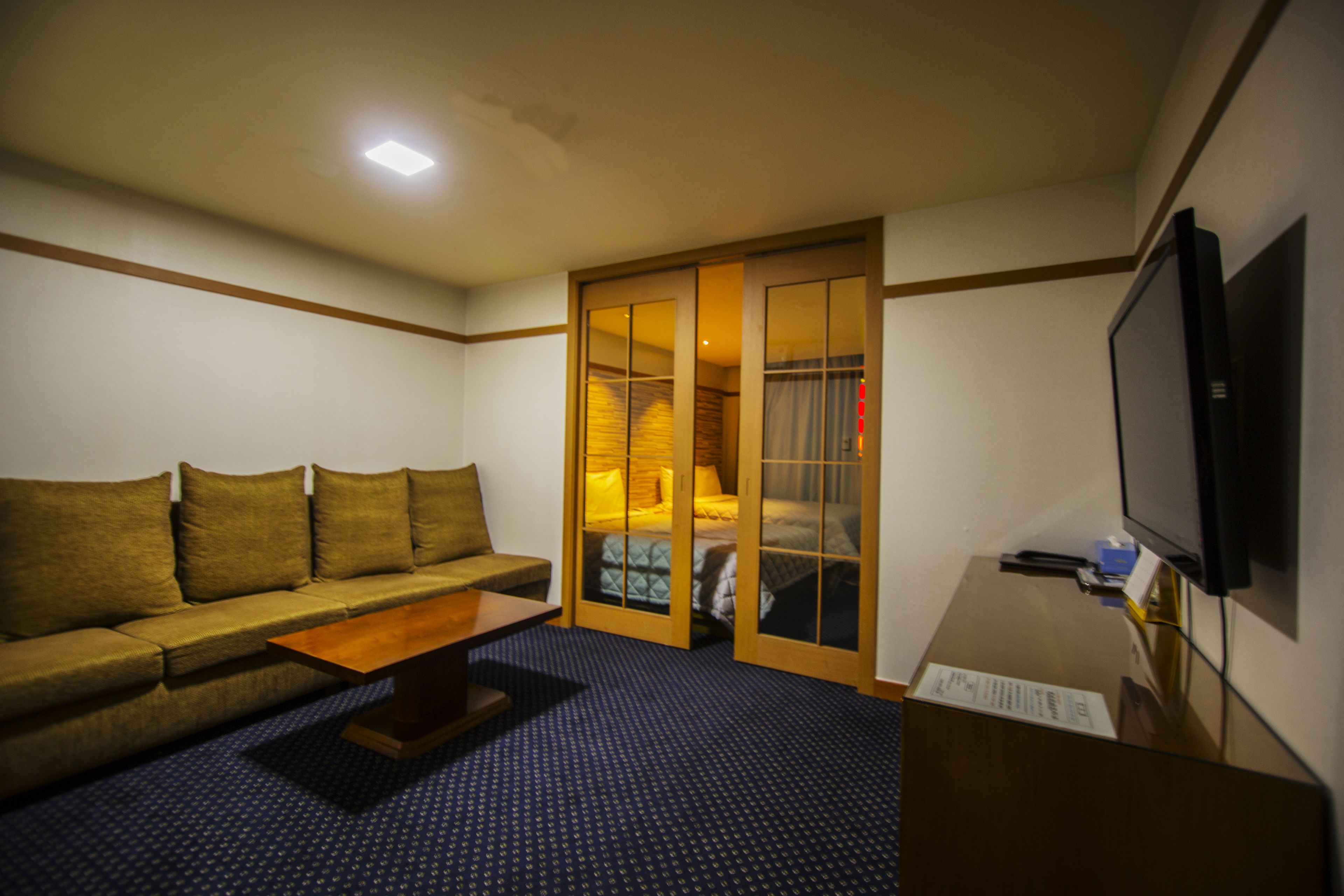 Habitació d'hotel amb un sofà, una taula de centre de fusta, una televisió i una porta corredissa que dona a un dormitori.