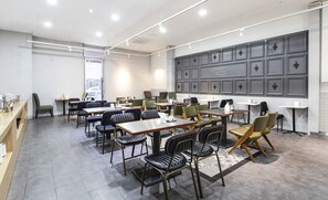 Una sala de conferencias moderna con varias mesas y sillas, una pared grande de color gris y vistas de la ciudad a través de un ventanal.
