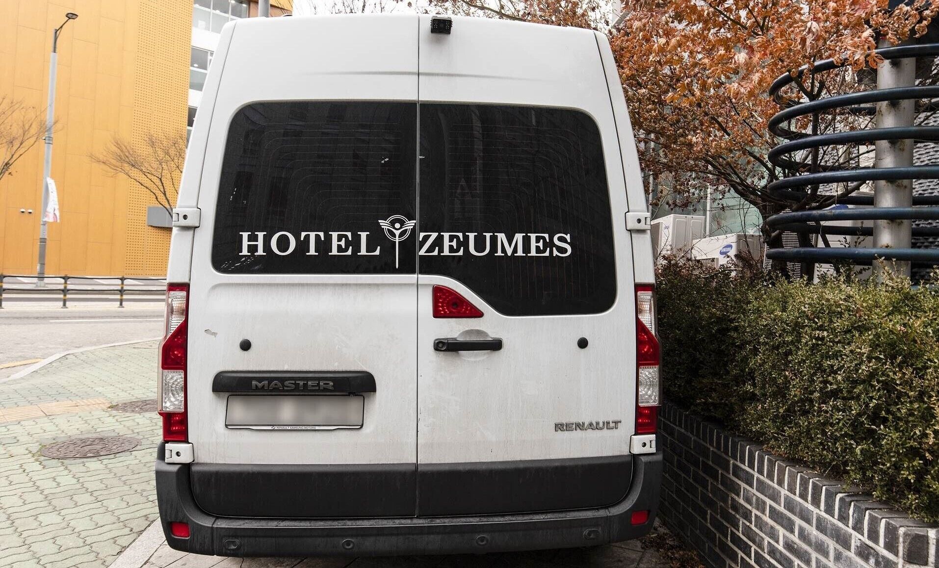 La parte trasera de una furgoneta blanca Renault Master con el texto "HOTEL ZEUMES" en la ventanilla trasera.