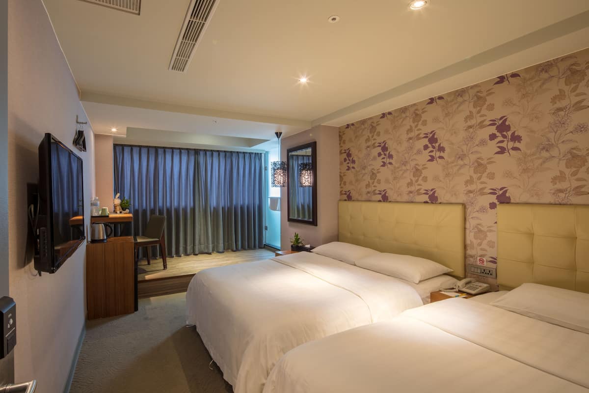 A hotel room with two beds, a desk with a chair, a television, and a window with curtains.