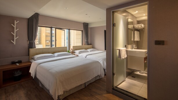 A modern hotel room with two beds, a bedside table, a bench, a large window with curtains, and a glass-enclosed bathroom. - Urtrip Hotel (Taipei)