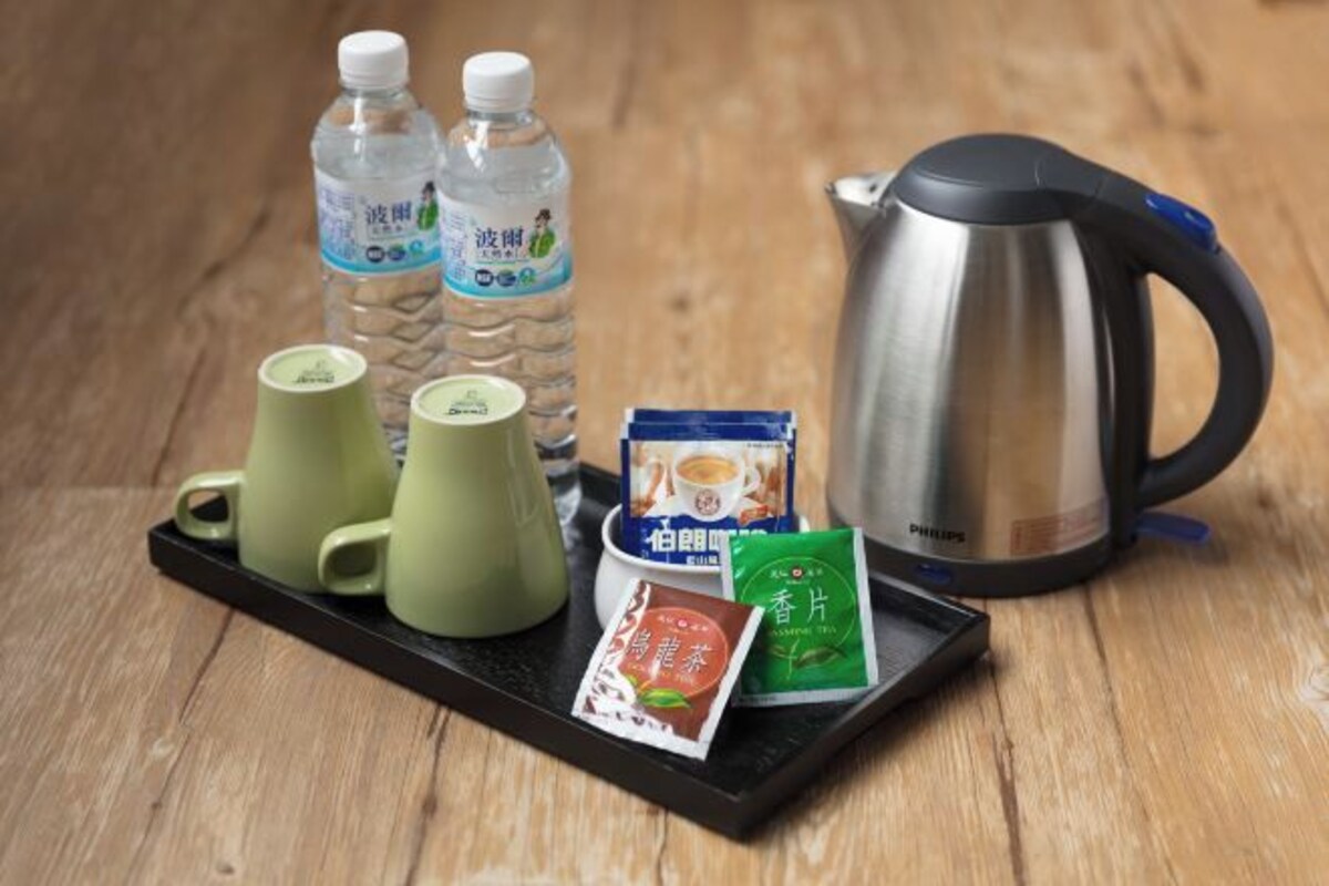 A tray with a kettle, two water bottles, two green cups, a packet of tea, and a packet of coffee.