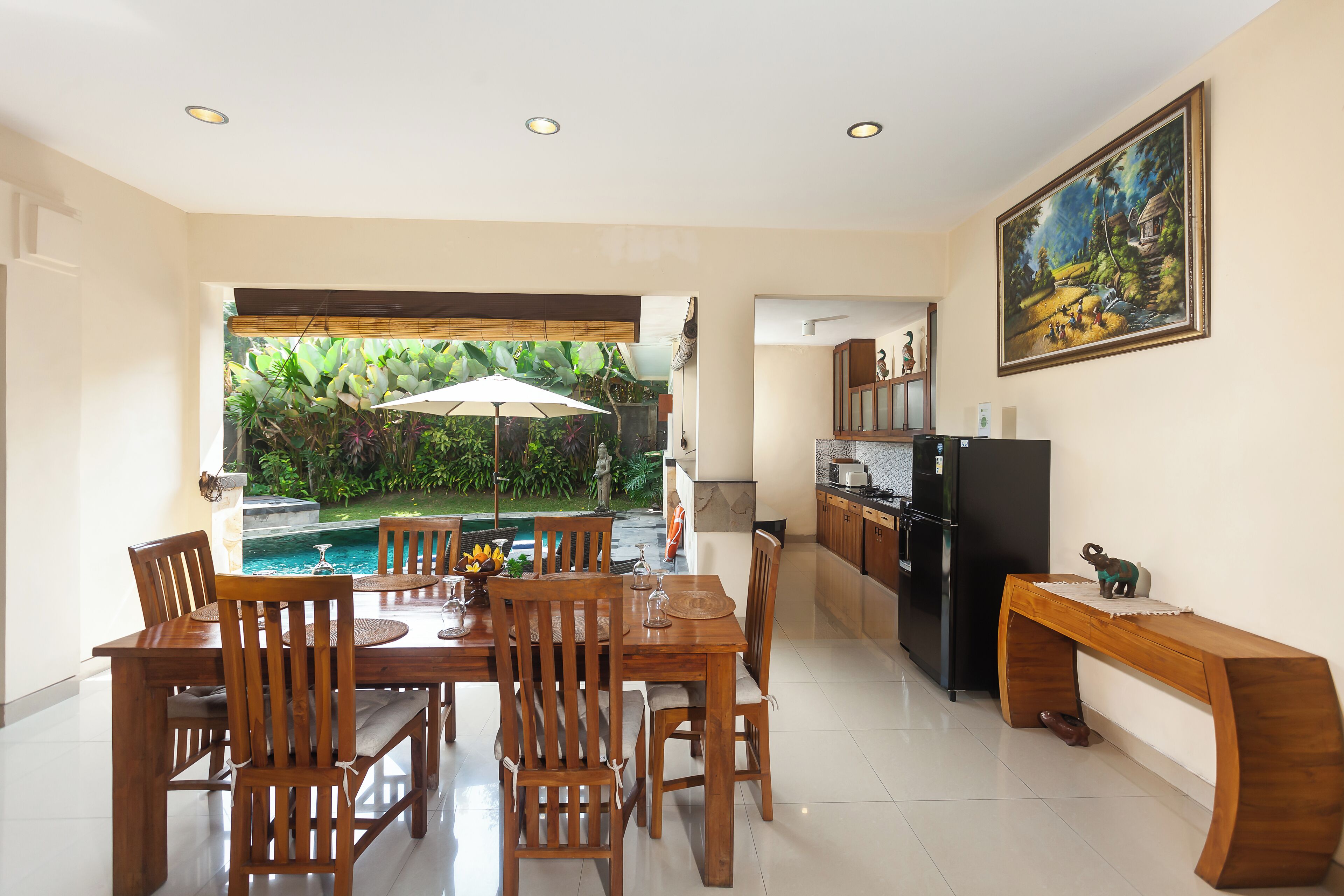 Un espace repas avec vue sur la piscine, doté de meubles en bois et d’un coin cuisine équipé d’un réfrigérateur.