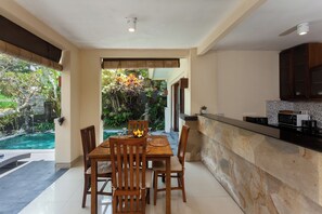 A dining area with a pool view, a kitchen with dark cabinets, and a stone countertop. - Kadiga Villas Ubud by GenuineHost (Ubud)