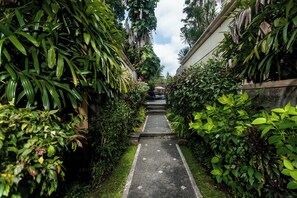 A narrow pathway flanked by lush greenery and a concrete wall. - Kadiga Villas Ubud by GenuineHost (Ubud)