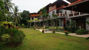 Un hotel moderno con un jardín bien cuidado, varios balcones y una variedad de plantas tropicales.