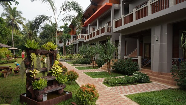 Un hotel moderno con un patio que cuenta con una fuente de agua, abundante vegetación y un sendero de ladrillo.