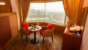 Habitación de esquina con un gran ventanal, sillas de mimbre con cojines rojos, una mesita redonda y un mueble de madera.
